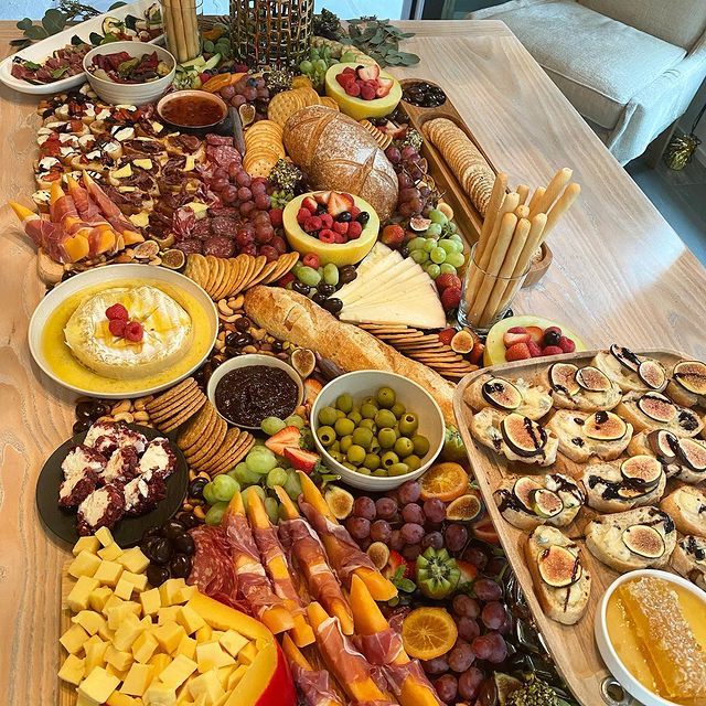 A table topped with a variety of food including cheese , grapes , bread and crackers.