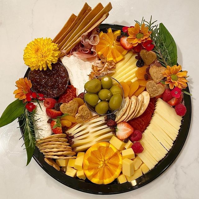 A black plate topped with a variety of fruits and cheeses