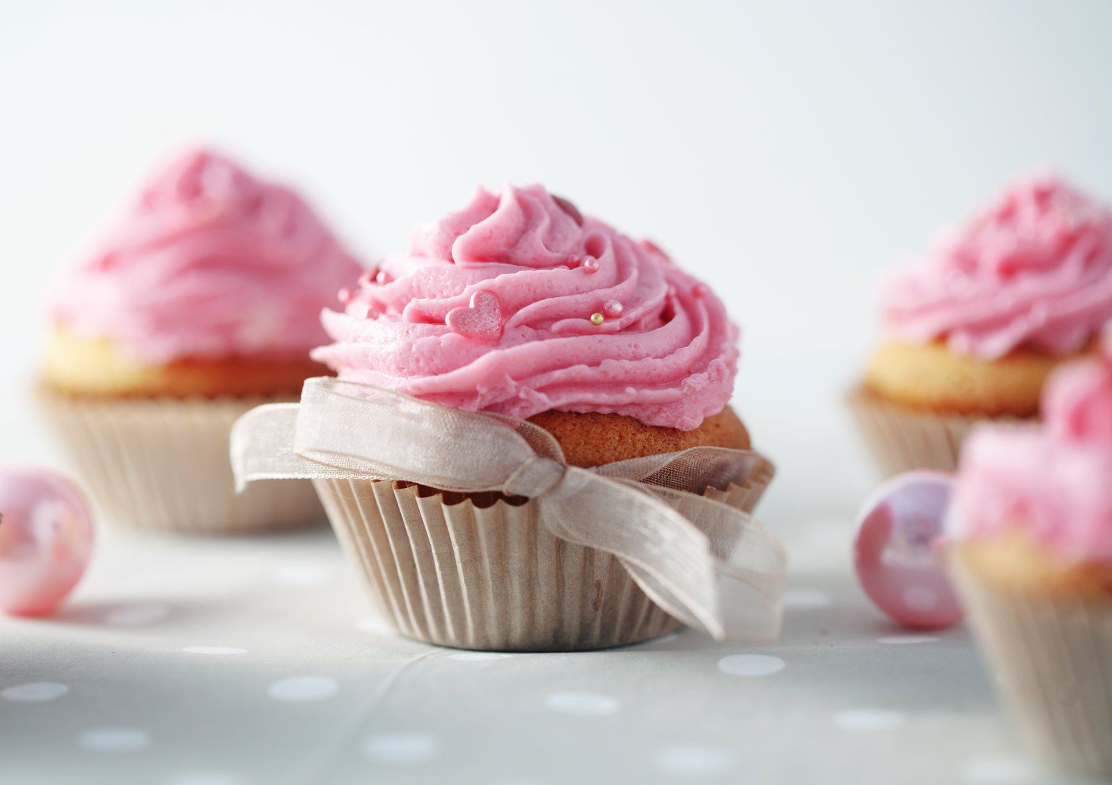 Three cupcakes with pink frosting and bows on a table.