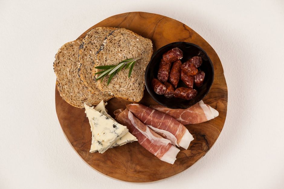 A wooden cutting board topped with bread , cheese , ham and sausage.