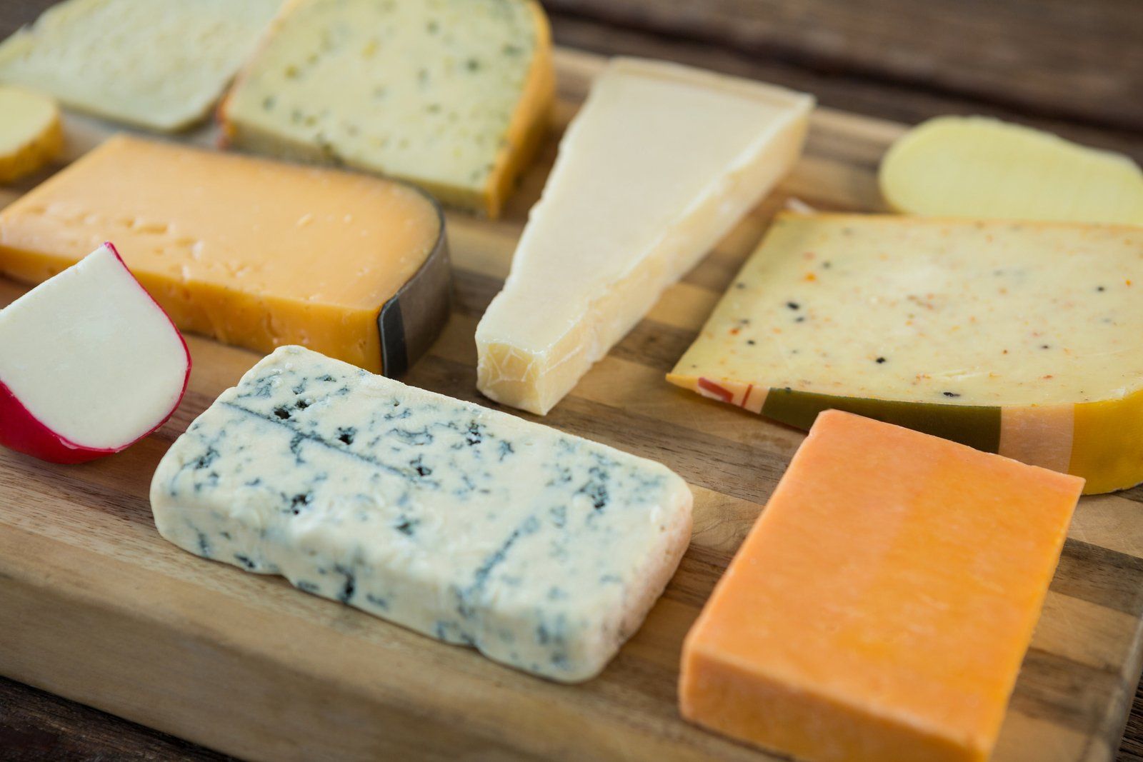 There are many different types of cheese on the cutting board.