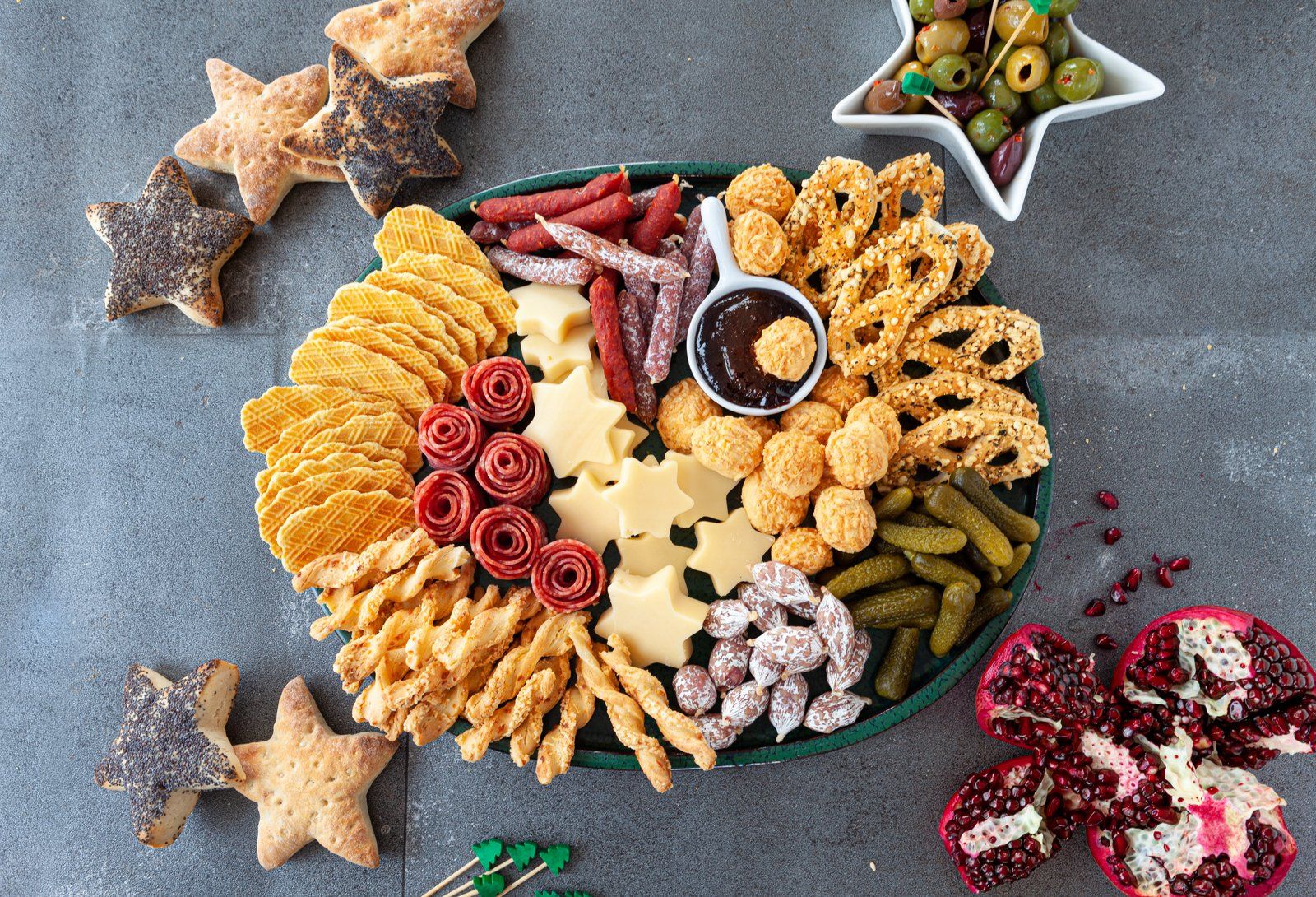 A tray of food with pretzels , crackers , cheese , olives and other snacks on a table.