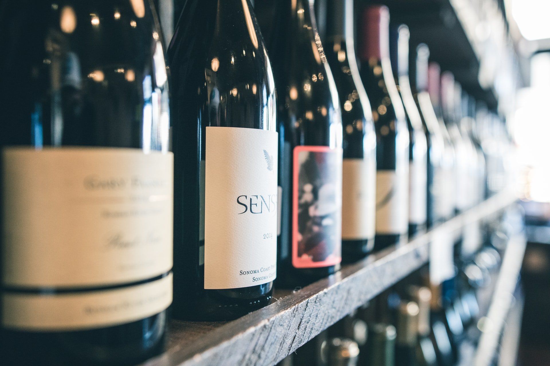 A row of wine bottles are lined up on a wooden shelf.