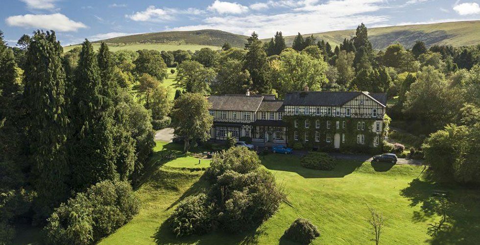 A hotel set within beautiful grounds, surrounded by trees and hills.