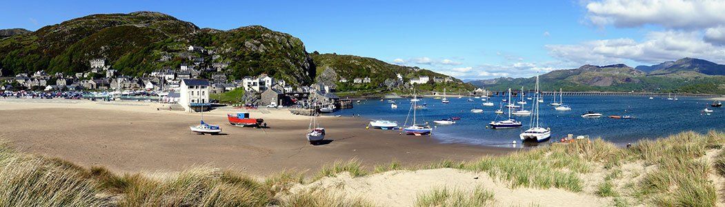 Welsh seaside town with small boats on the beach and in the water.