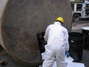 Man is safety suit working beside a large tank