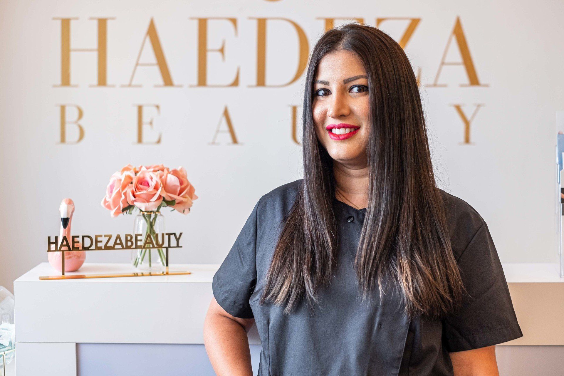 Eine Frau steht vor einem Schild mit der Aufschrift „Haedza Beauty“.