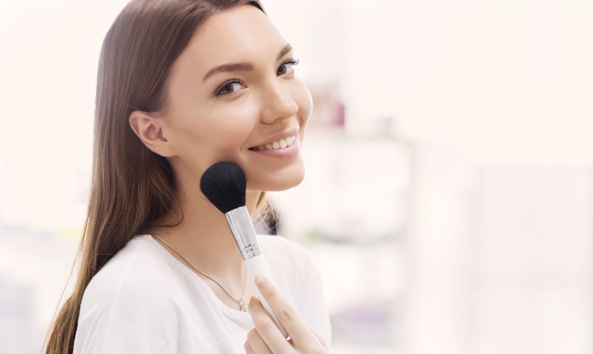 Eine Frau trägt mit einem Pinsel Make-up auf ihr Gesicht auf.