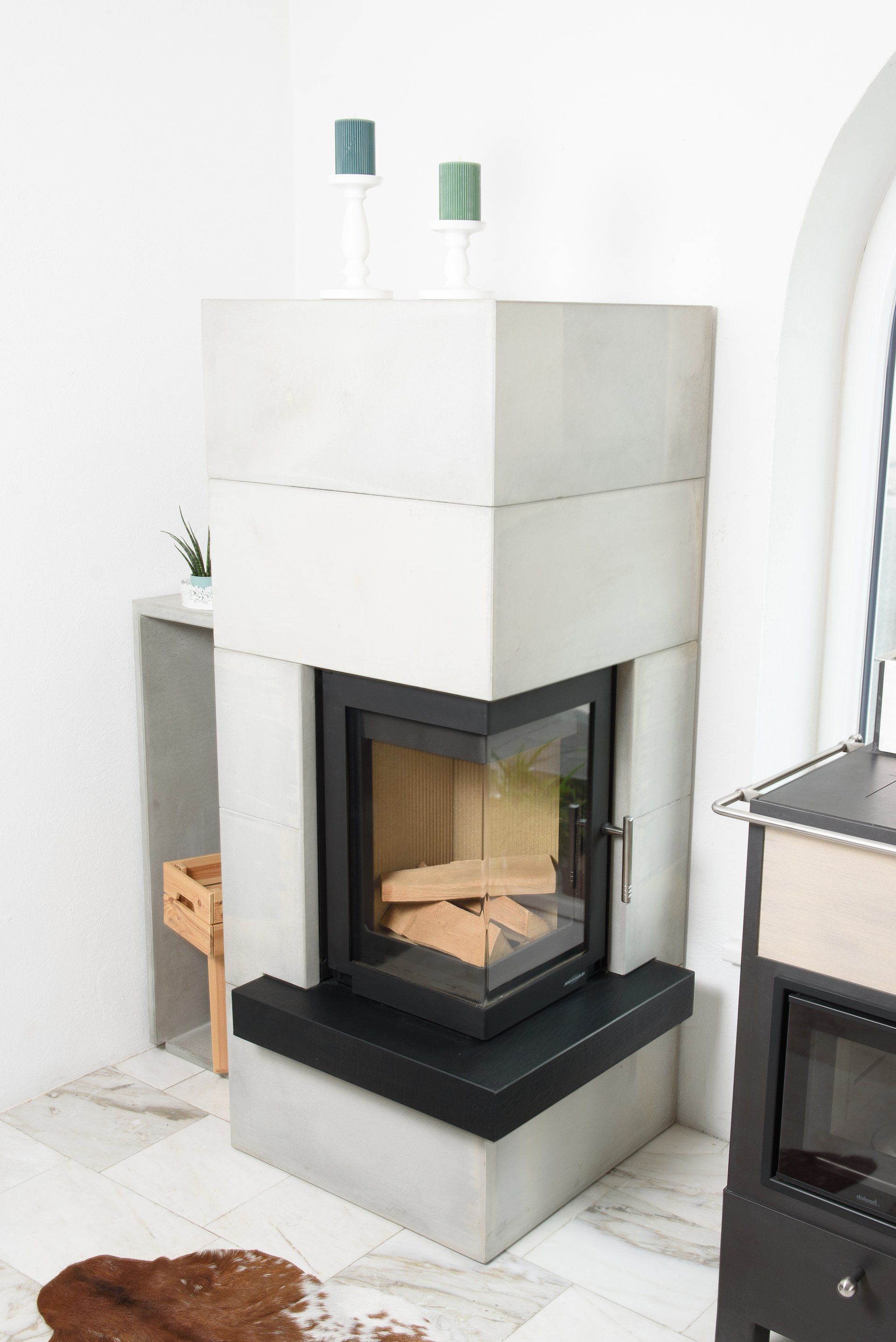 Moderner weißer Kamin mit schwarzem Glasfeuerraum in einem hellen Wohnzimmer