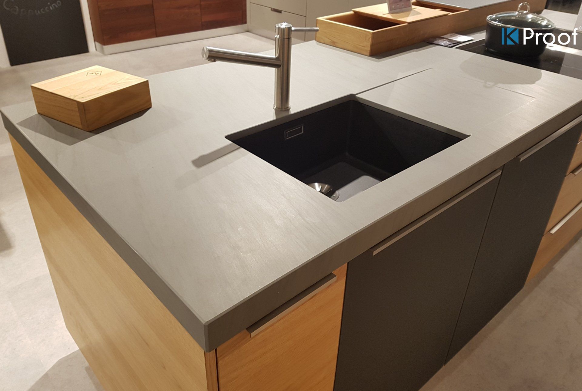 Moderne Kücheninsel mit grauer Arbeitsplatte, eingebautem schwarzem Spülbecken und hölzernen Aufbewahrungsboxen darauf.