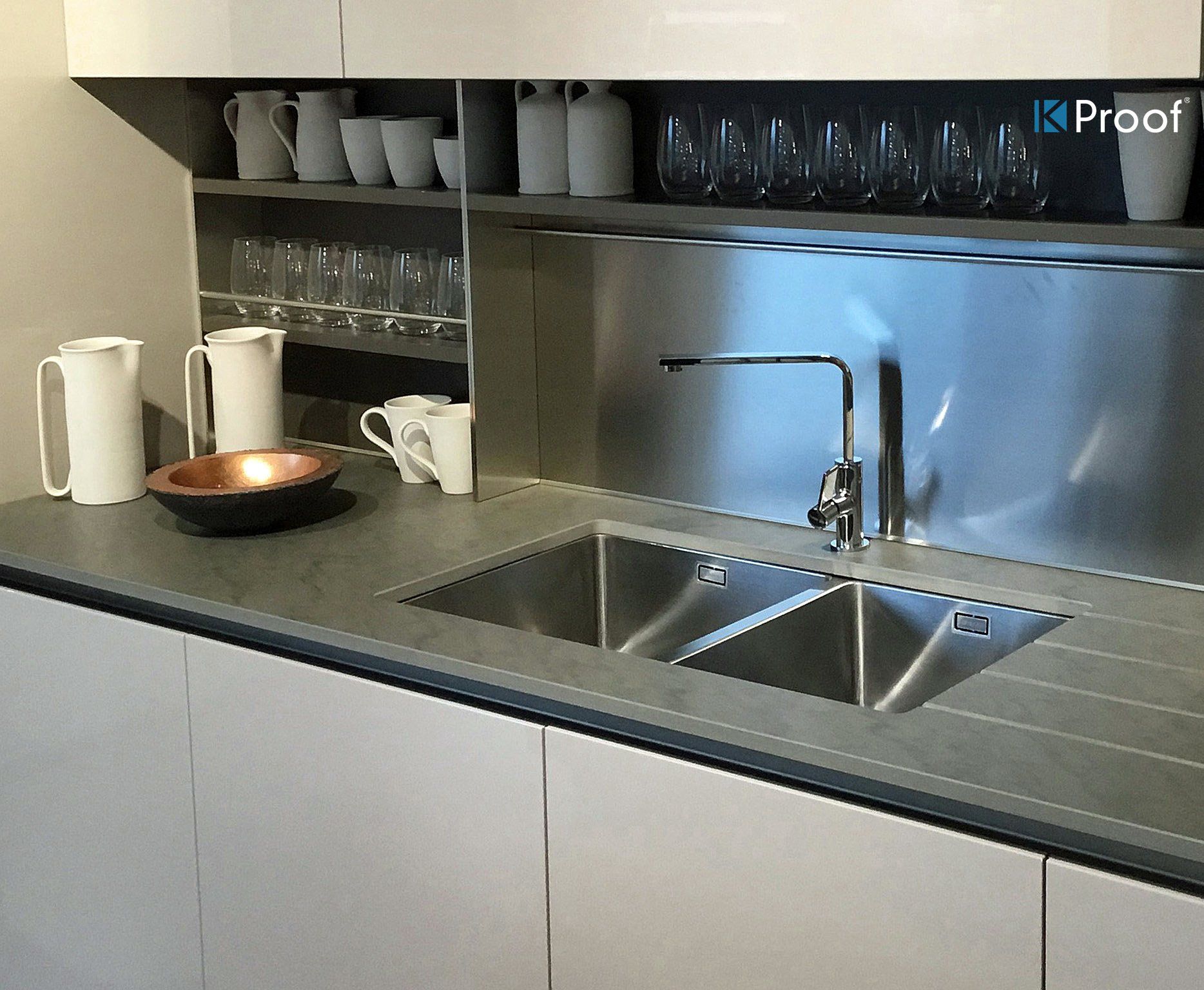 Moderne Küchenspüle mit Edelstahl-Arbeitsplatte, Schränken, Bechern, Gläsern und einer Schüssel auf der linken Seite.