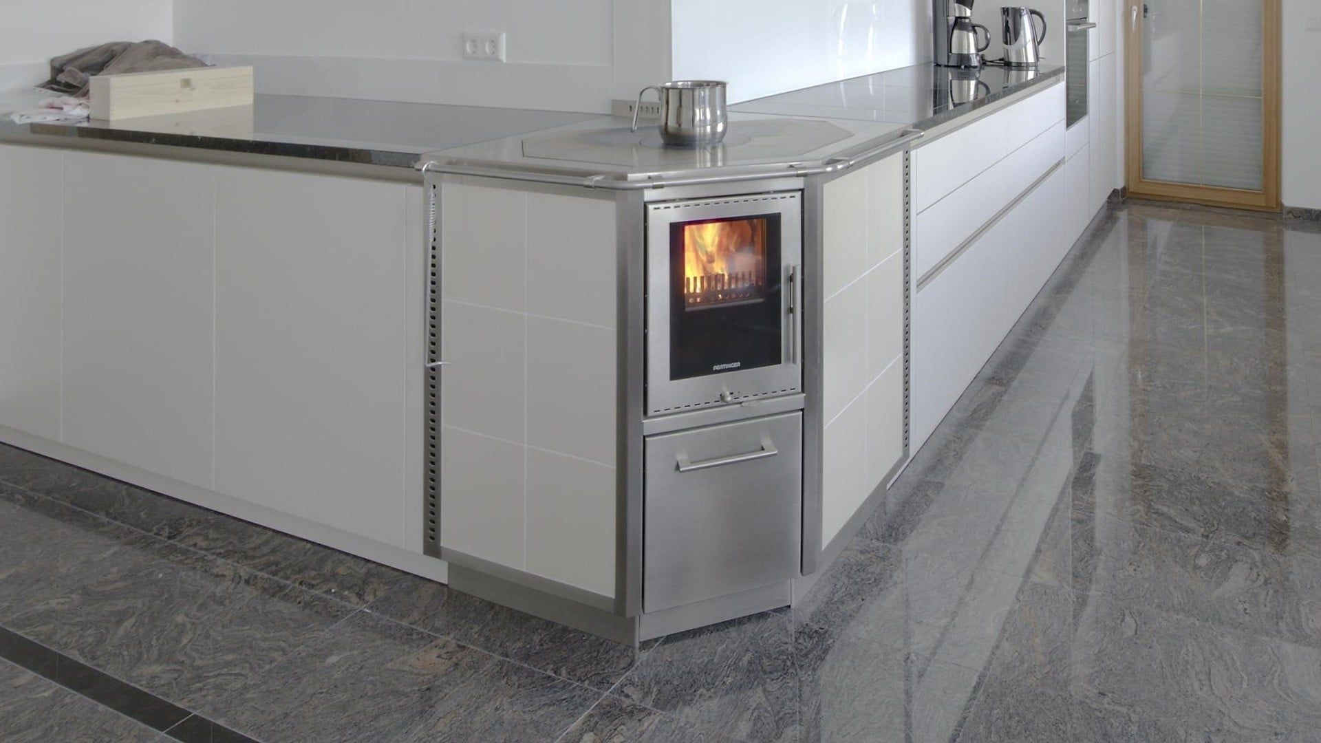 Moderne Küche mit einem eingebauten Edelstahl-Backofen, der in einer grauen Stein-Arbeitsinsel leuchtet.