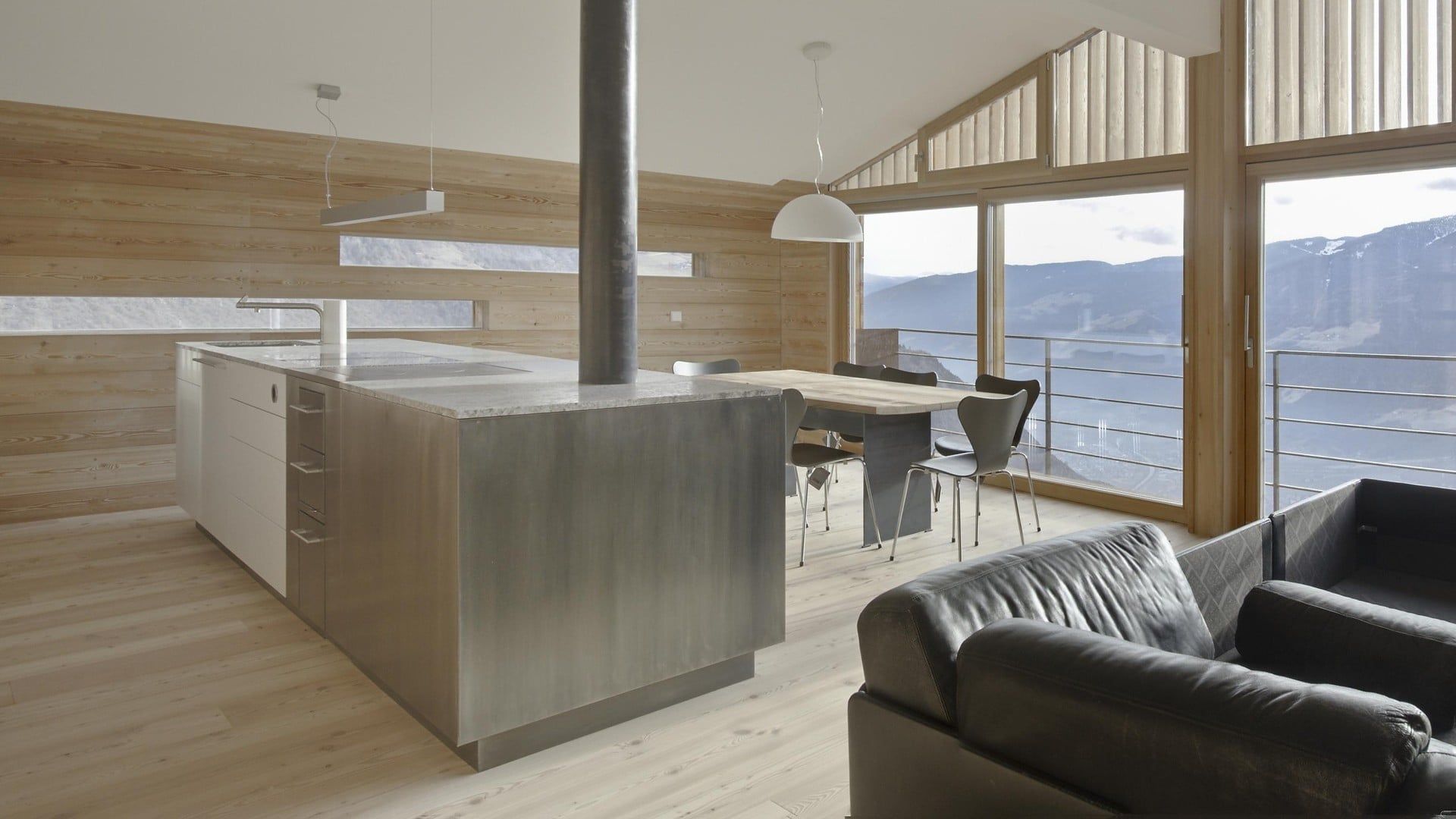 Moderne, offene Loftküche mit Wohnbereich, Holzelementen und großen Fenstern mit Bergblick