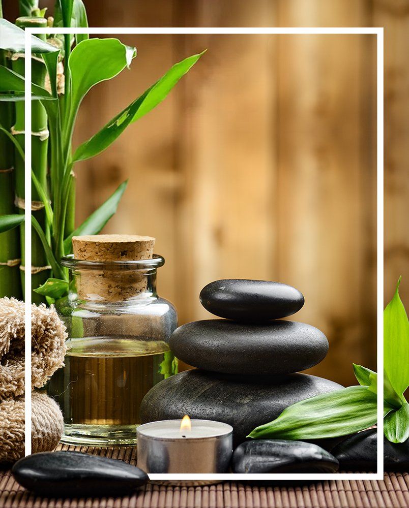 A bottle of oil, a stack of rocks, a candle and a bamboo plant are on a table.