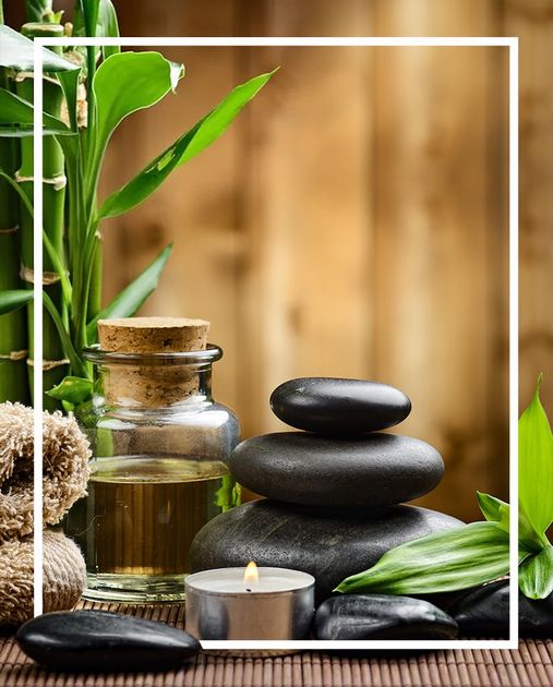 A bottle of oil, a stack of rocks, a candle and a bamboo plant are on a table.