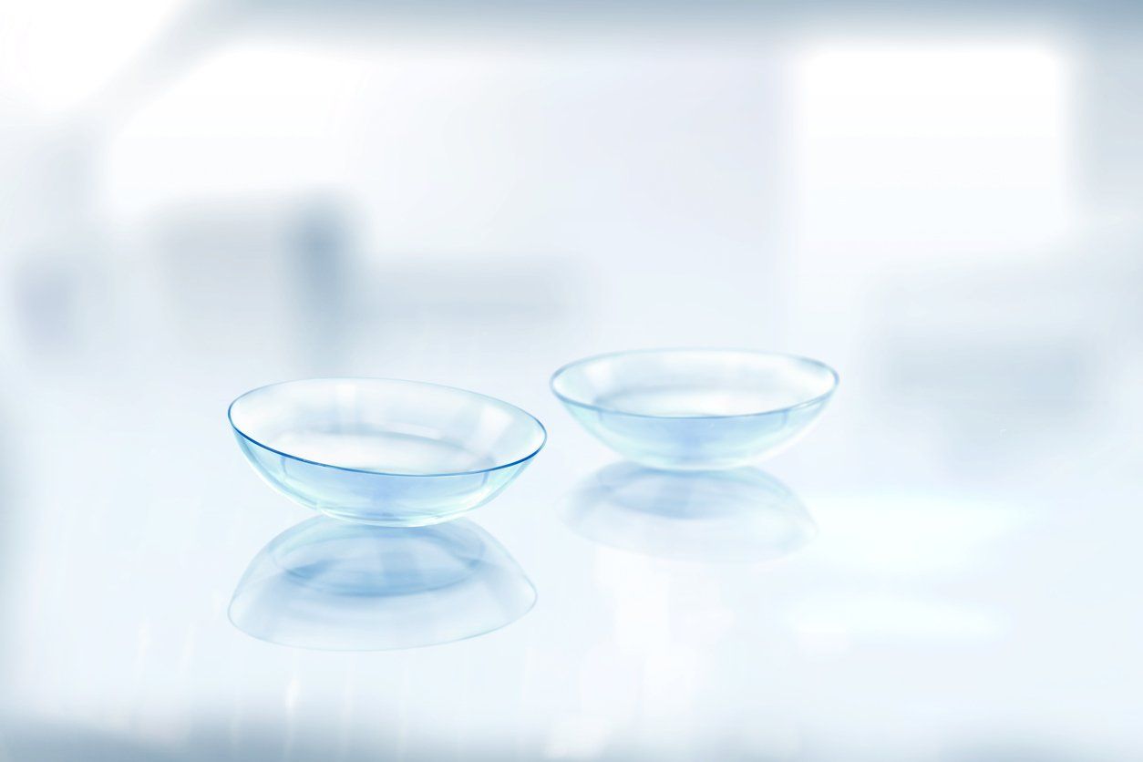 Two clear contact lenses on a reflective surface, in a bright, blurred environment.