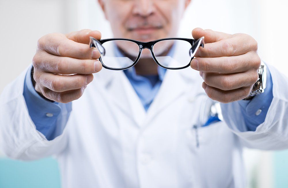 Doctor in white coat holds up eyeglasses.