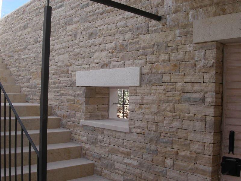 Kamienny mur z małym oknem, schodami i metalową balustradą.