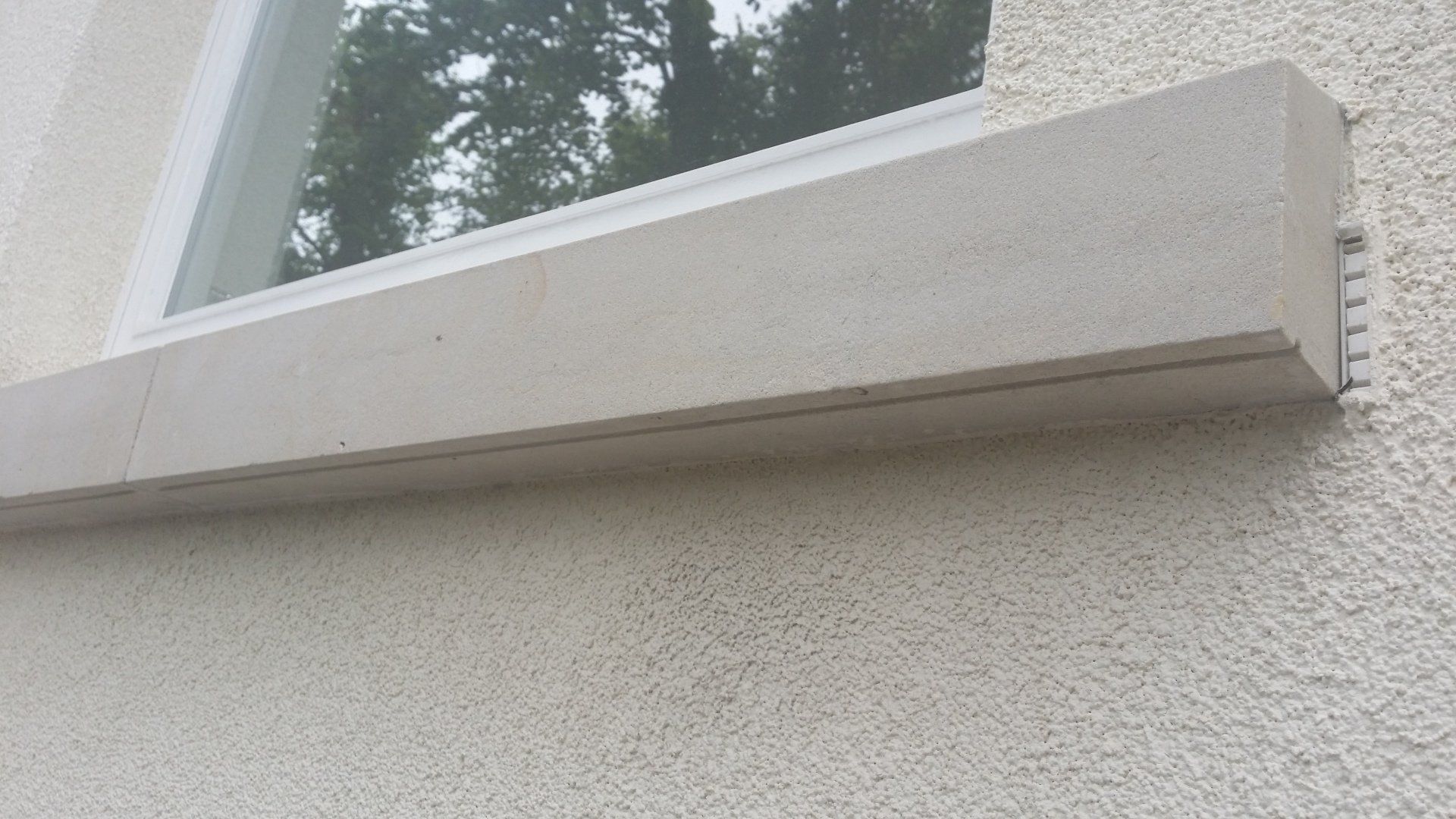Jasny kamienny parapet pod oknem osadzonym w ścianie ze stiuku.