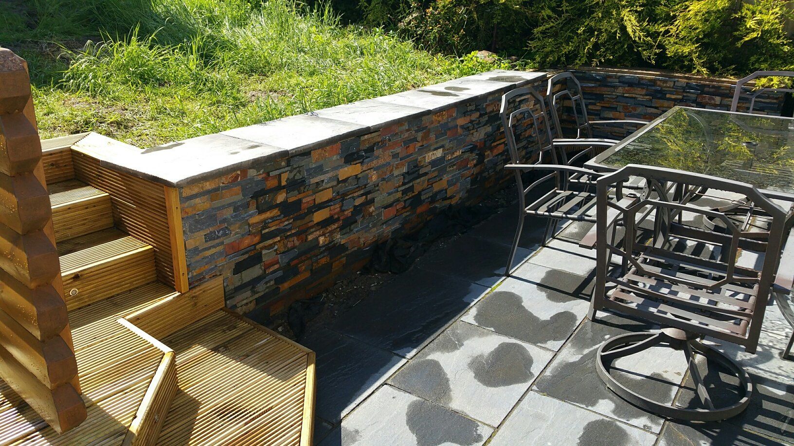 Patio na świeżym powietrzu z kamiennym murem, schodami i meblami ogrodowymi.