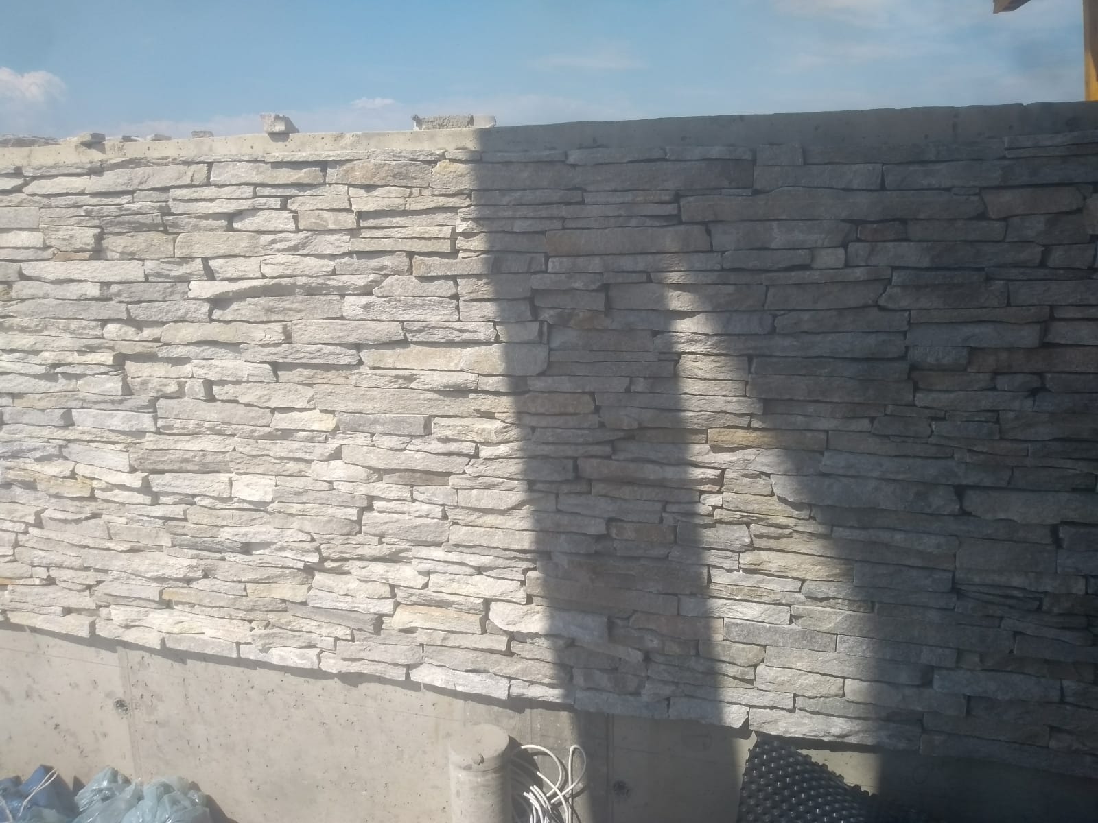 Kamienny mur w odcieniach jasnoszarego i jasnobrązowego, z długimi, prostokątnymi kamiennymi elementami. Cień pada po prawej stronie.