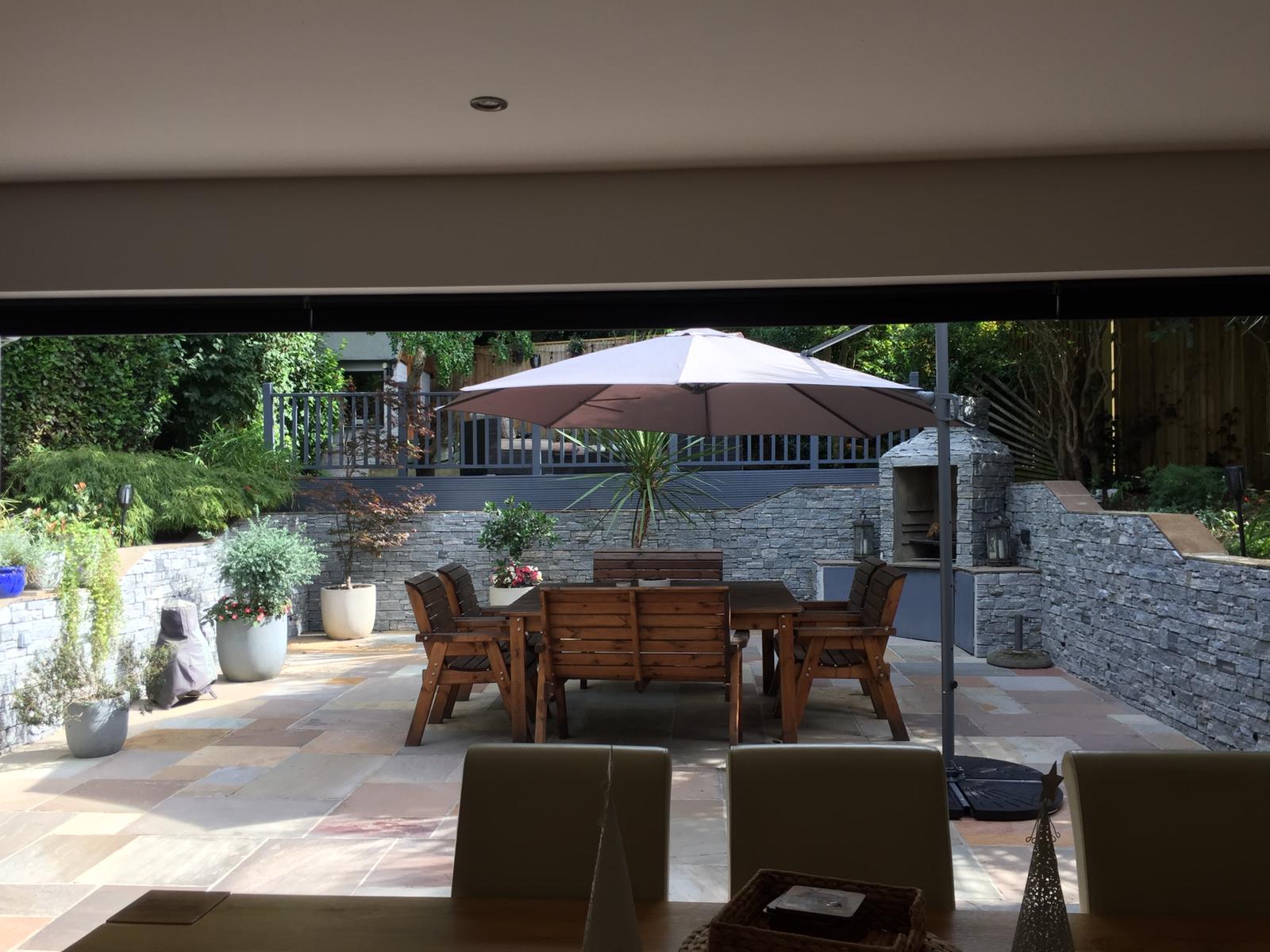 Patio na świeżym powietrzu z drewnianymi meblami, parasolem i kamiennymi ścianami.