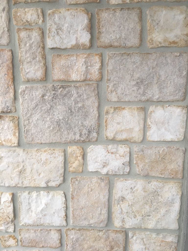 Mur kamienny z różnorodnych prostokątnych i kwadratowych bloków, w kolorze beżowym i jasnobrązowym, z szarą zaprawą.