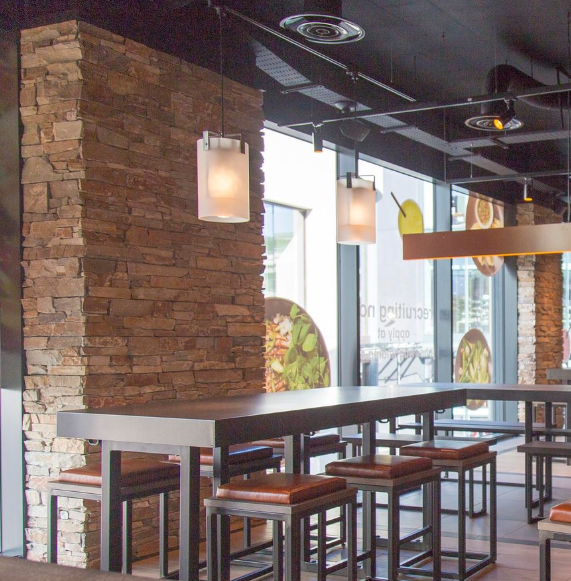 Wnętrze restauracji z kamienną ścianą i długim stołem ze stołkami.