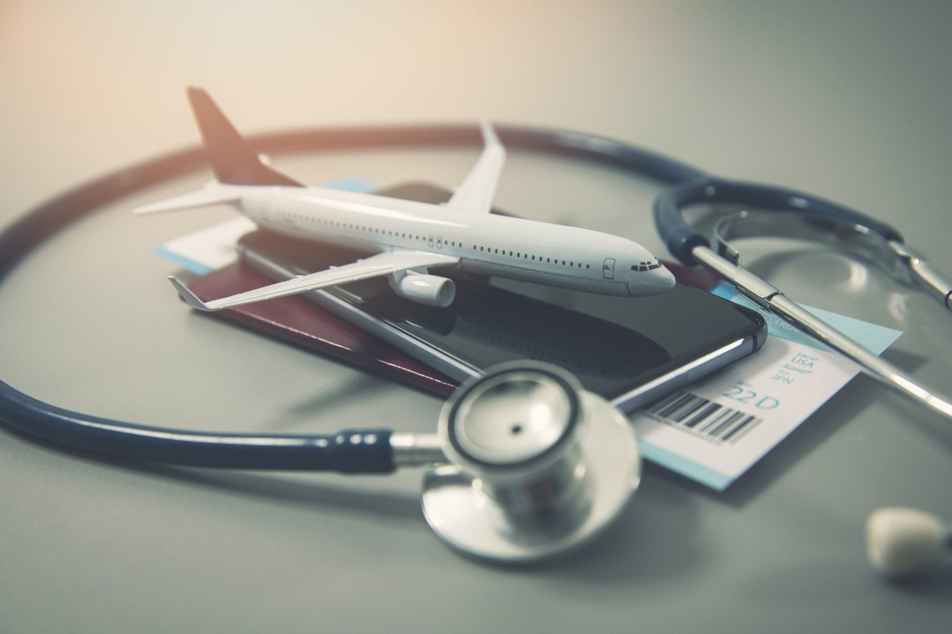Toy airplane on travel documents and phone, surrounded by stethoscope, suggesting travel health.