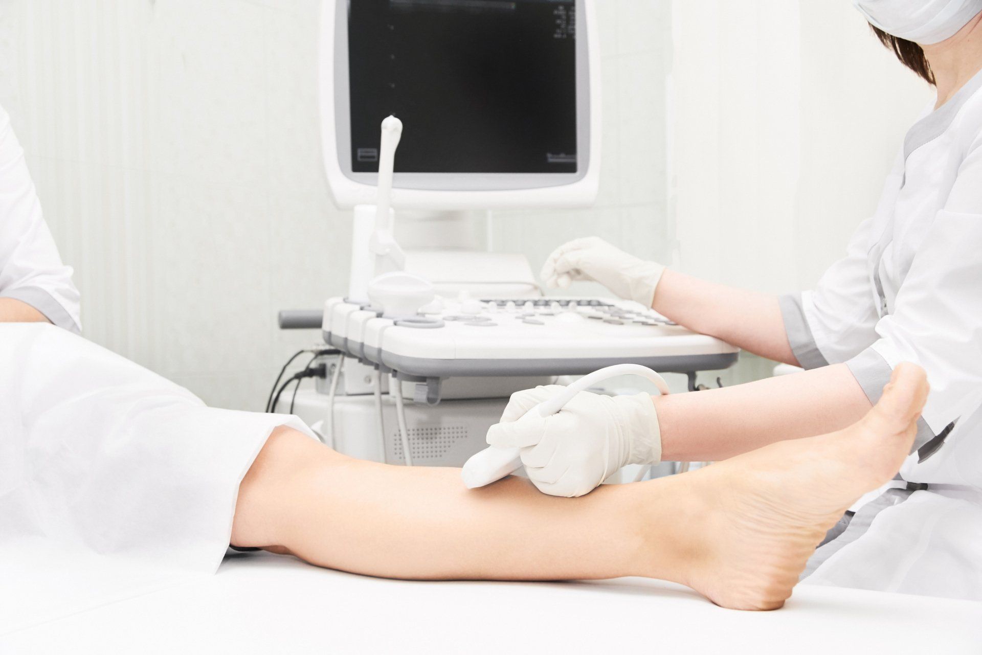 Medical professional using ultrasound on a patient's leg. In a clinic, white coats, gloves, and ultrasound machine are visible.