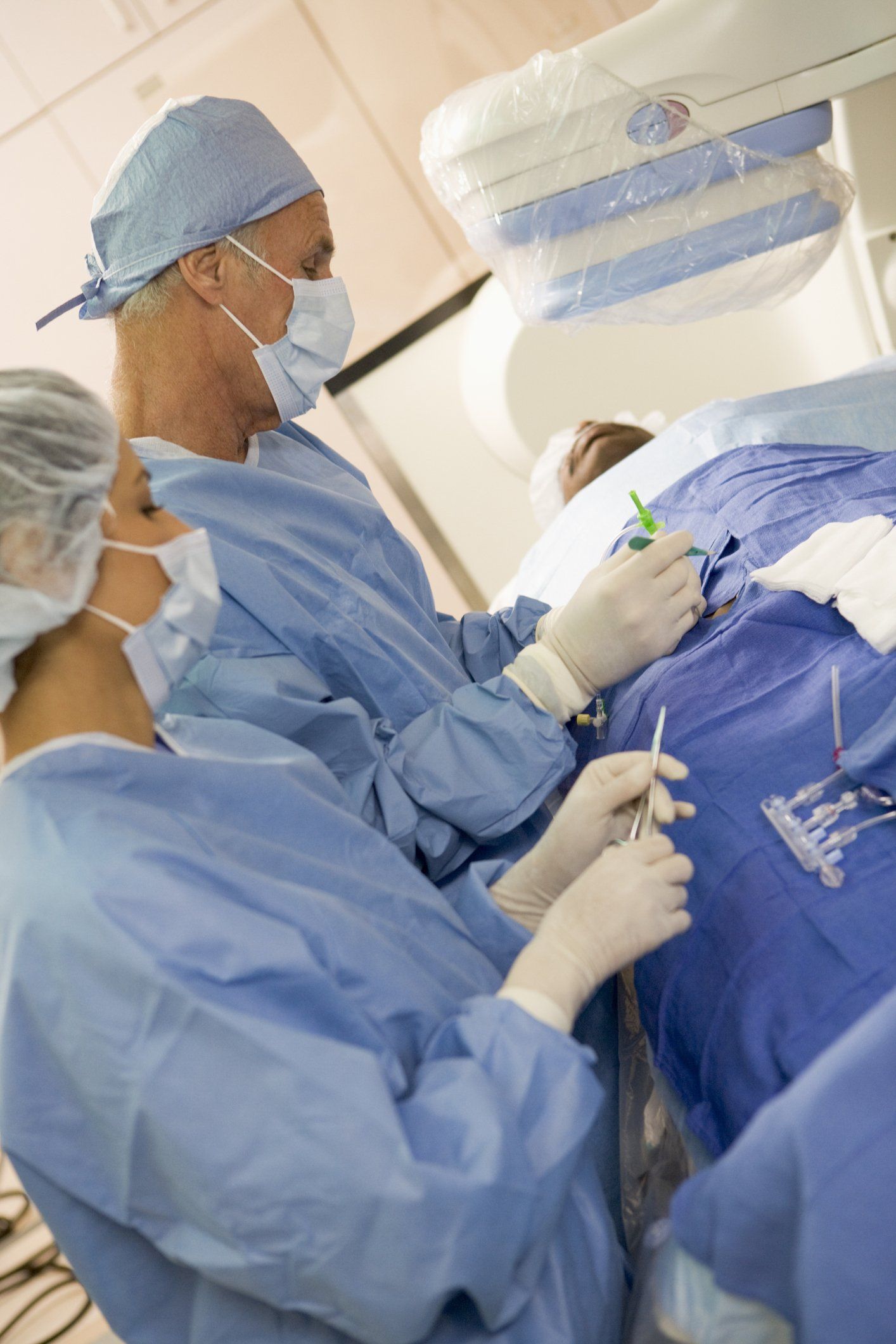 Surgeons in blue scrubs perform a medical procedure on a patient in a sterile operating room.