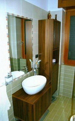 Bagno con mobiletto in legno, lavandino e mobile alto. Specchio con cornice piastrellata, piastrelle verdi e beige.