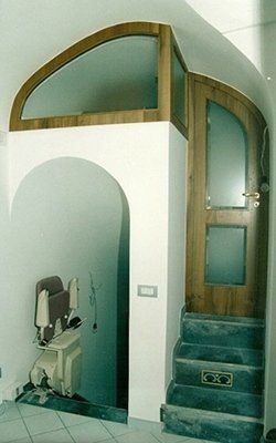 Ingresso con scale che conducono a una porta in legno con vetro smerigliato e una finestra ad arco. Un montascale si trova nella nicchia.