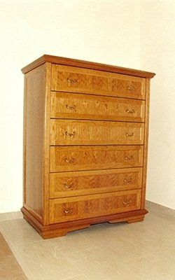 Cassettiera in legno a sei cassetti in una tonalità marrone chiaro, contro una parete bianca e un pavimento piastrellato.