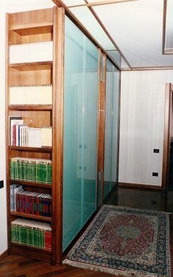 Libreria in legno accanto a pannelli in vetro smerigliato e un tappeto sul pavimento scuro di una stanza.