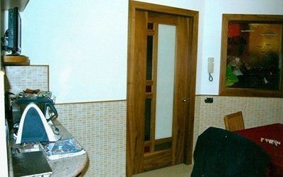 Una porta di legno con pannello di vetro conduce a una stanza. Il bancone della cucina è dotato di elettrodomestici e un tavolo da pranzo.