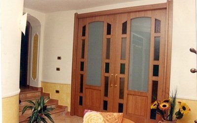 Doppie porte in legno con pannelli in vetro; ingresso con gradini e piante.