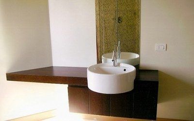 Bagno moderno con mobile lavabo sospeso in legno scuro, lavandino bianco rotondo e rubinetto alto.