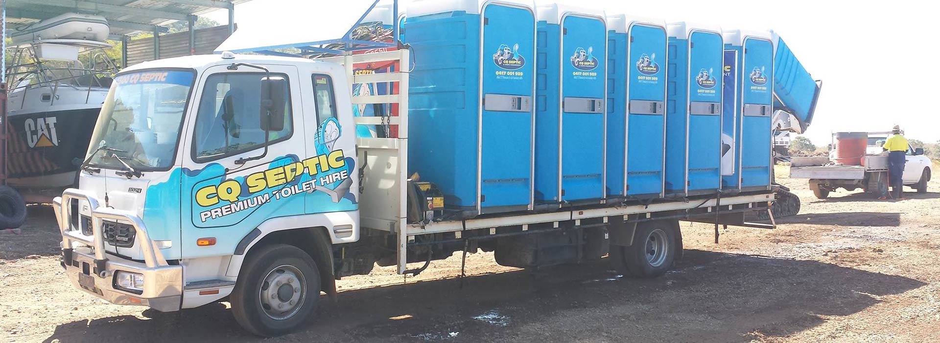 A truck filled with blue portable toilets is parked in a gravel lot.