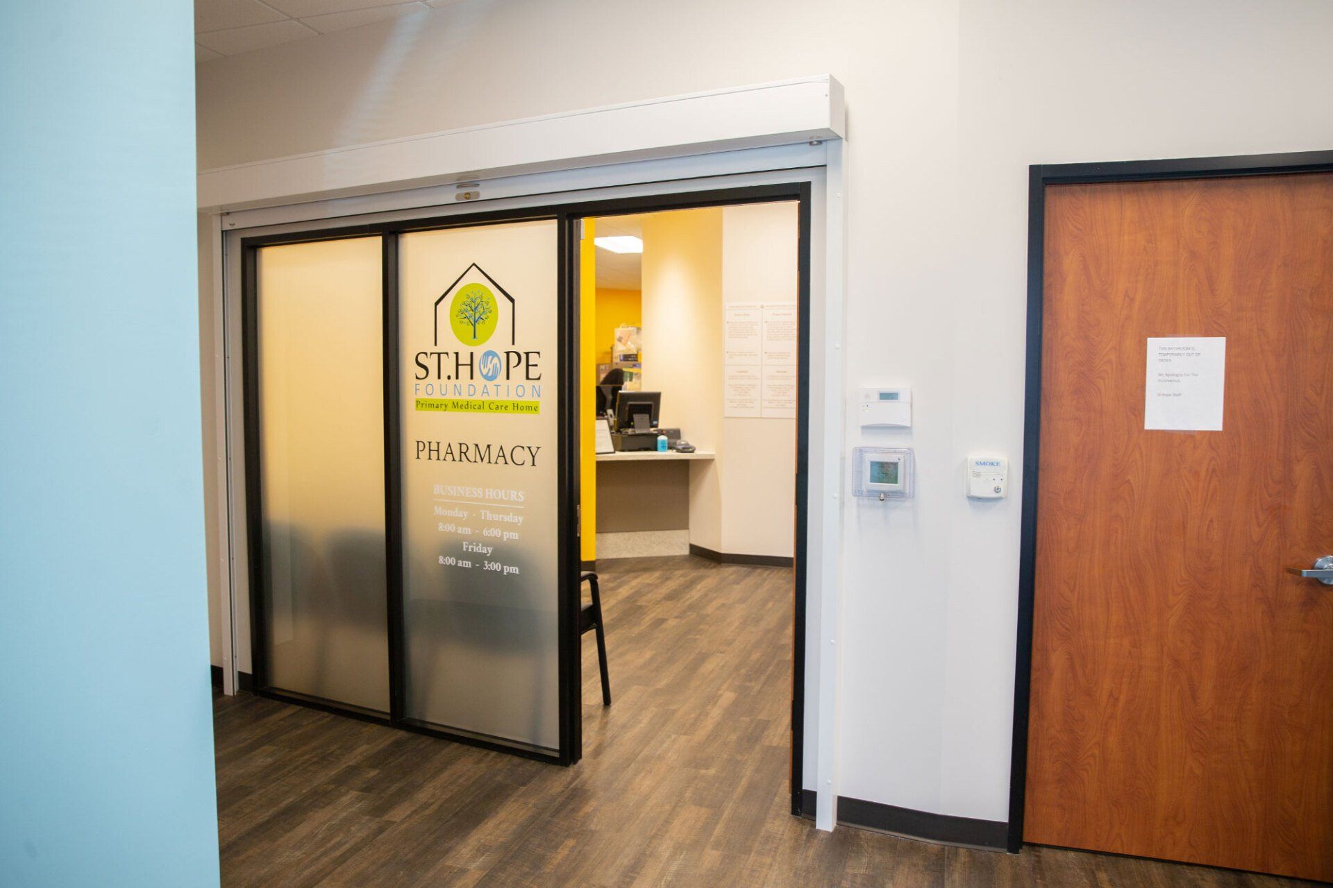Entrance to a pharmacy with a sliding glass door displaying the St. Hope Pharmacy logo, set in a neutral-colored hallway.