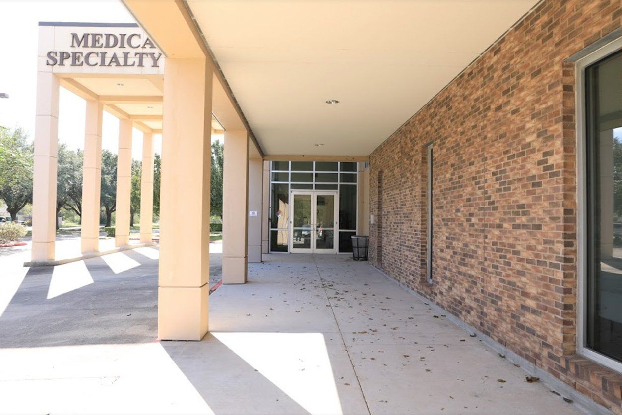A walkway leading to a Medical Specialty building entrance with tan pillars and a stone brick wall.