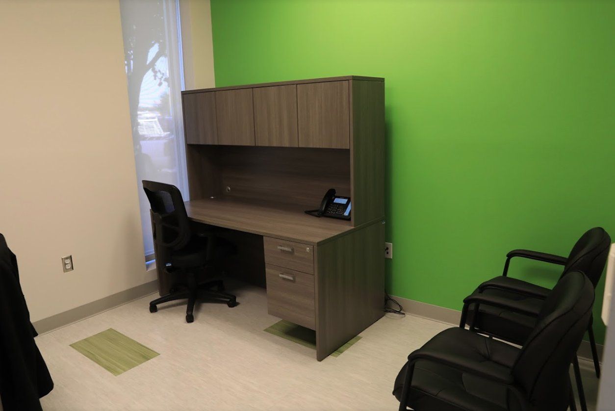 A modern office features a gray desk with cabinets, a black chair, and two black guest chairs against a lime green wall.