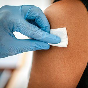 A medical professional in blue gloves wipes a person's upper arm with a white antiseptic swab.