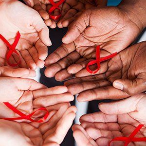 Several open hands hold small red ribbons, the symbol of HIV/AIDS awareness.