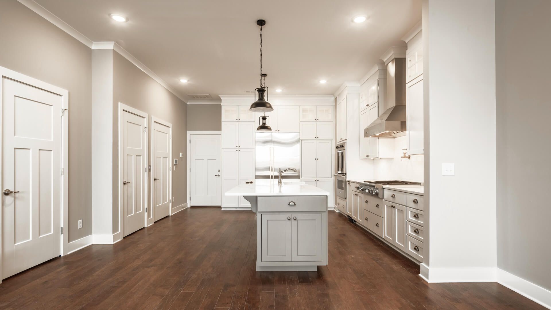 A bright, modern kitchen with white cabinets, a central island, stainless steel appliances, and dark hardwood floors.