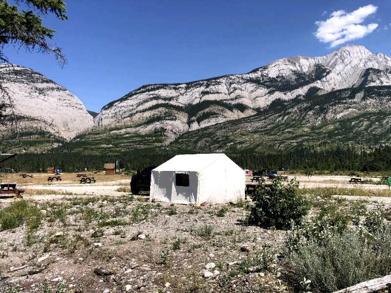 A white tent is in the middle of a field with mountains in the background