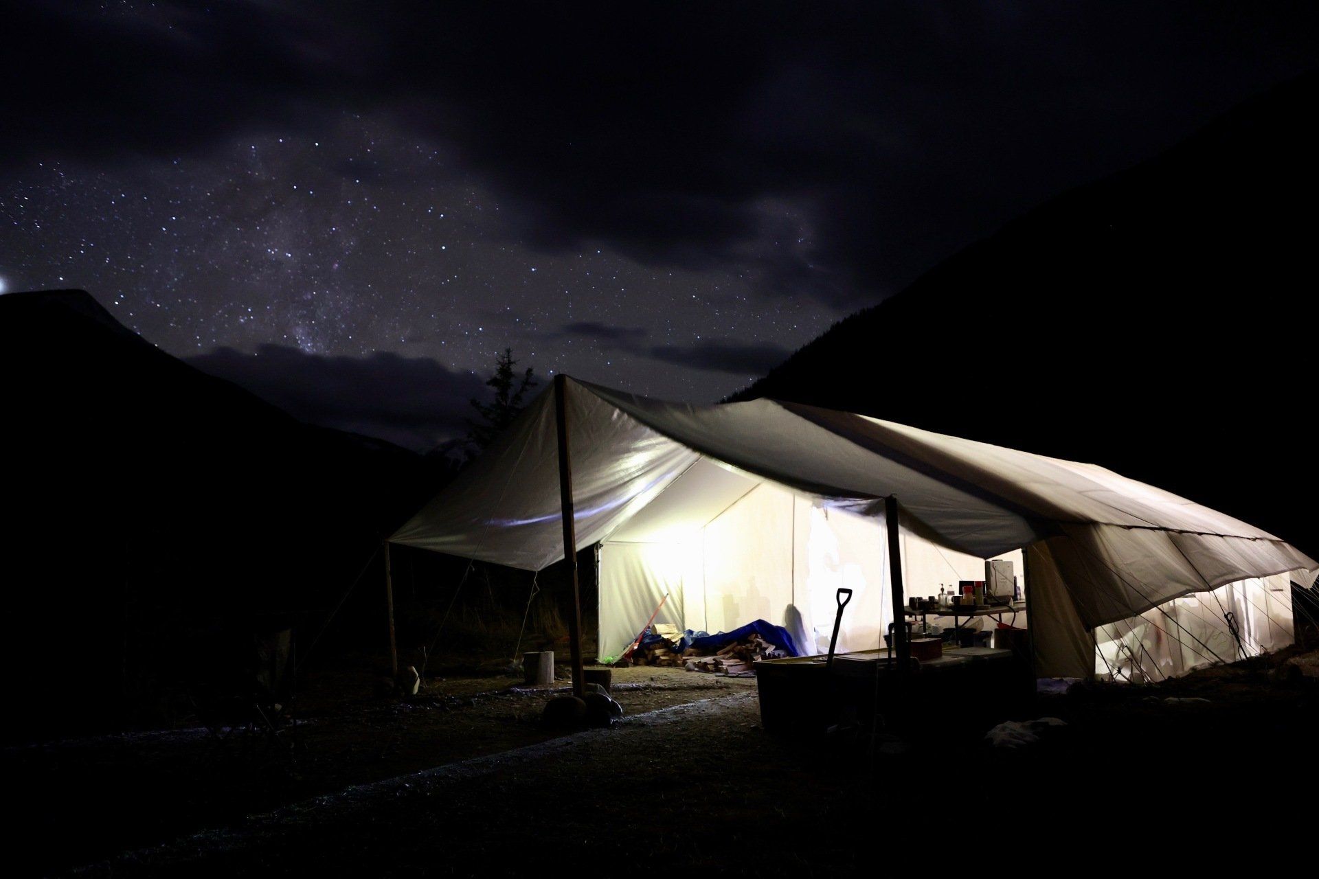 A tent is lit up at night under a starry sky.