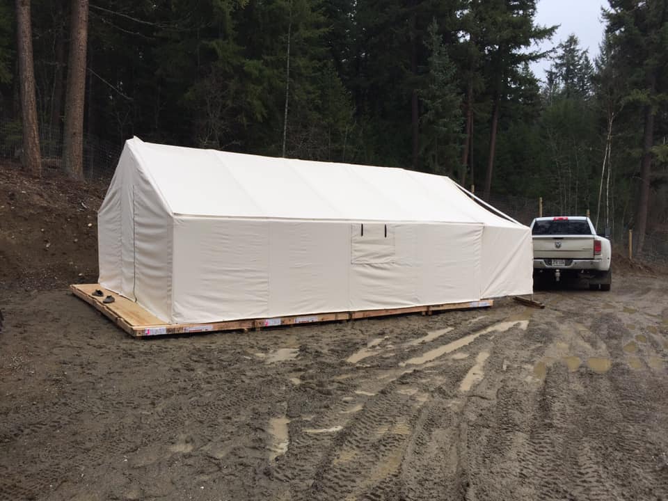 A large white tent is sitting in the middle of a dirt road next to a truck.