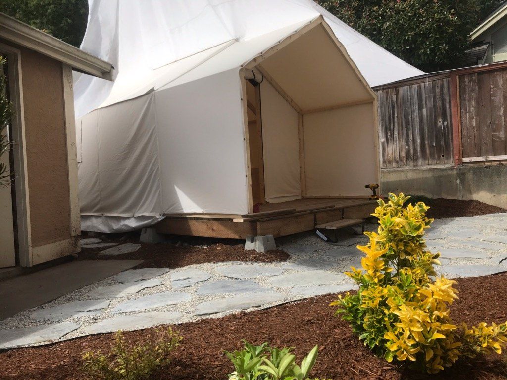 A white tent is sitting in the backyard of a house.