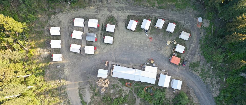 An aerial view of a campground with tents and trucks parked in a circle.